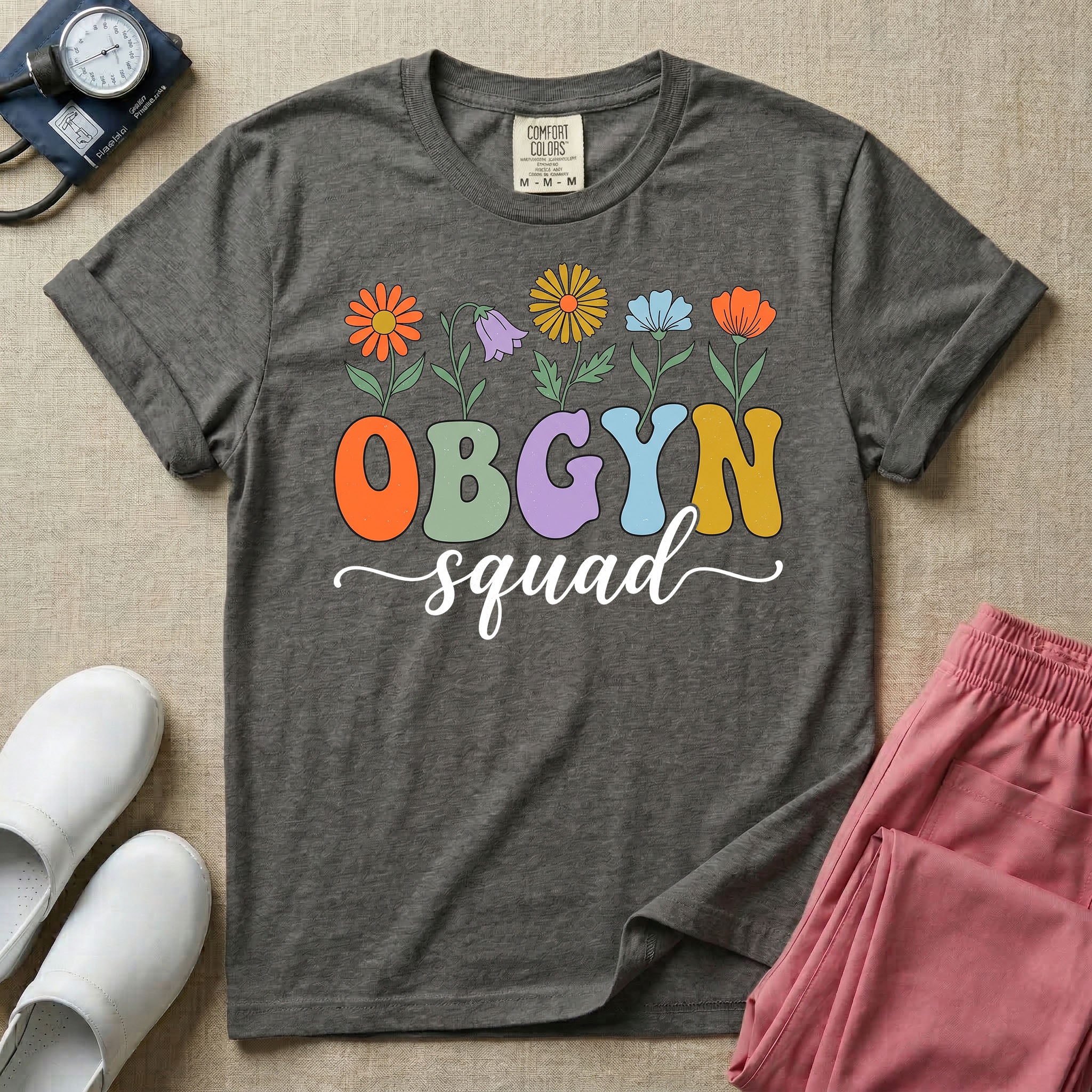 A retro floral graphic design for an OB-GYN unit featuring colorful retro flowers growing out of the letters OBGYN, with the word squad written below in a white cursive script.