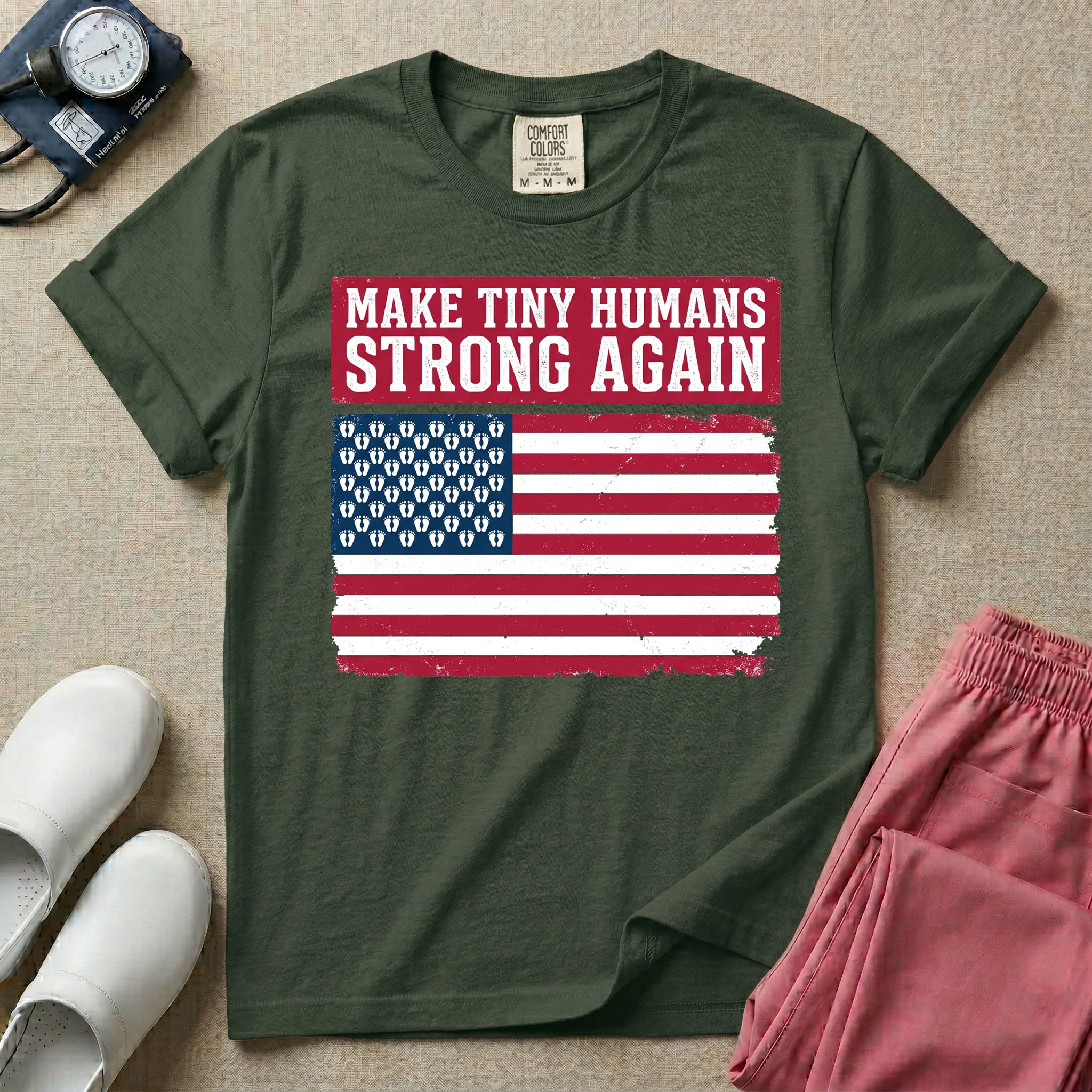 A patriotic graphic design for NICU nursing featuring the text MAKE TINY HUMANS STRONG AGAIN in white block letters against a distressed red background, positioned above a vintage American flag where the traditional stars have been replaced by rows of tiny white baby footprints.