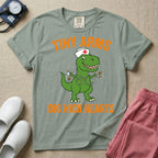 A funny neonatal intensive care unit t-shirt featuring an illustration of a green T-Rex dinosaur wearing a nurse cap and stethoscope, juggling a baby bottle and pacifiers, surrounded by distressed orange text that reads "TINY ARMS" at the top and "BIG NICU HEARTS" at the bottom.