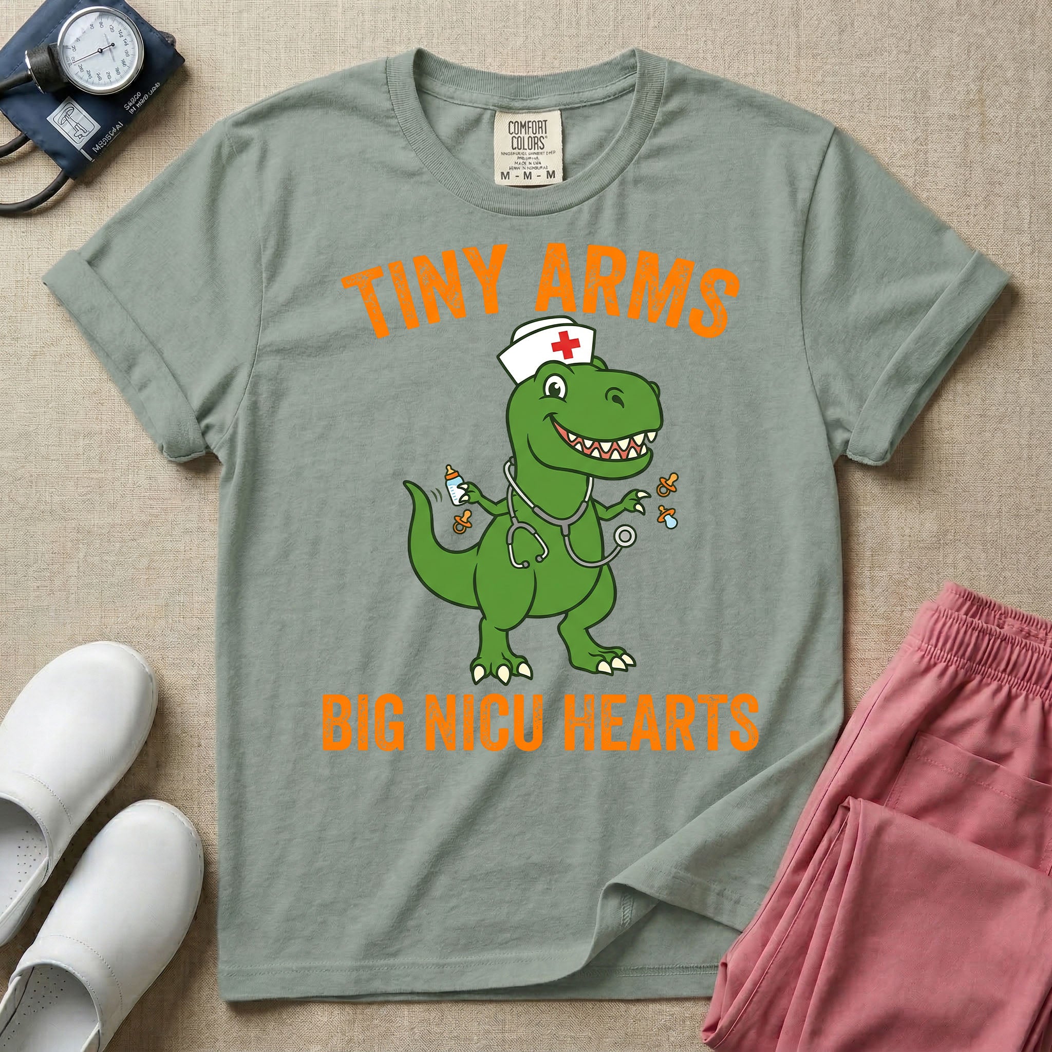 A funny neonatal intensive care unit t-shirt featuring an illustration of a green T-Rex dinosaur wearing a nurse cap and stethoscope, juggling a baby bottle and pacifiers, surrounded by distressed orange text that reads "TINY ARMS" at the top and "BIG NICU HEARTS" at the bottom.