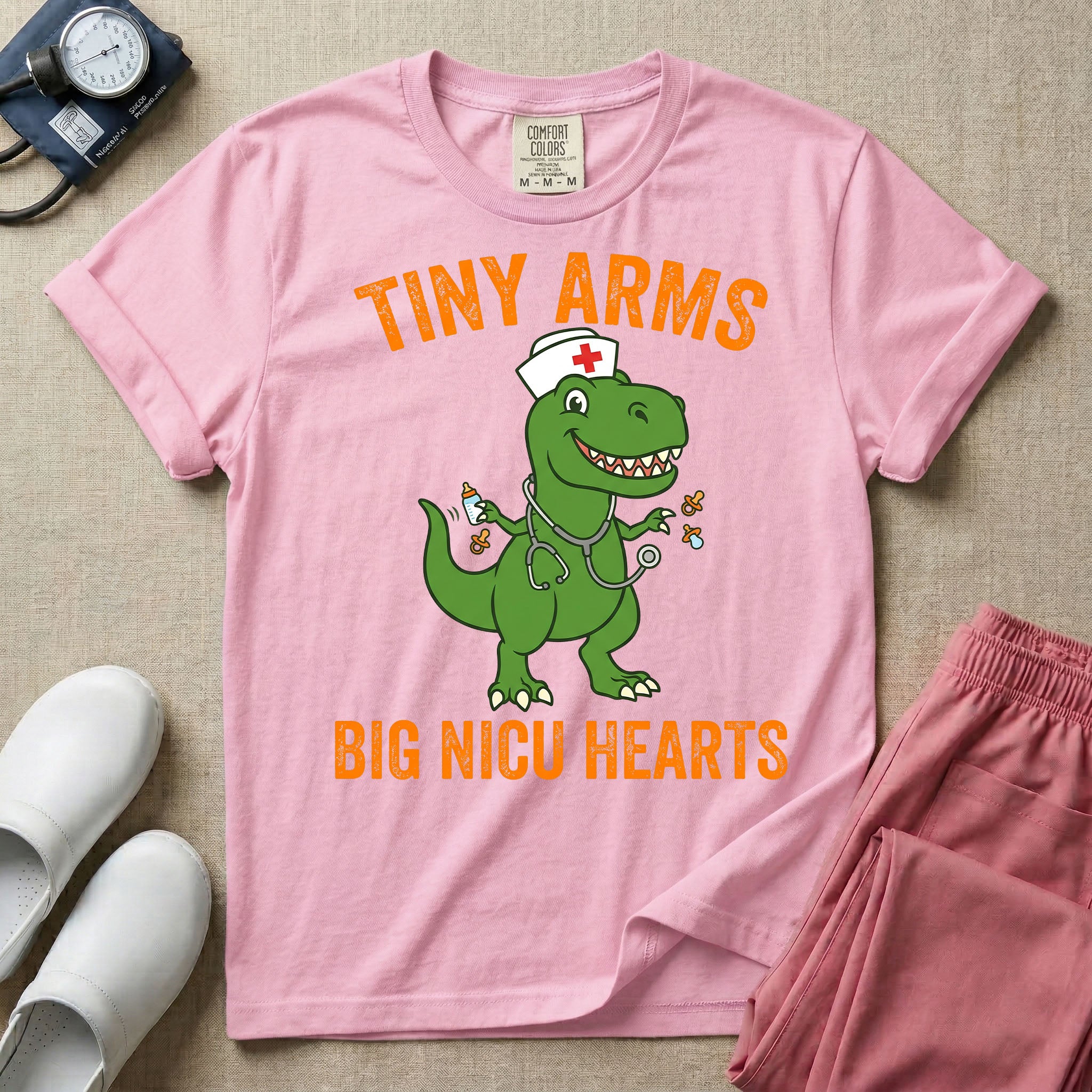 A funny neonatal intensive care unit t-shirt featuring an illustration of a green T-Rex dinosaur wearing a nurse cap and stethoscope, juggling a baby bottle and pacifiers, surrounded by distressed orange text that reads "TINY ARMS" at the top and "BIG NICU HEARTS" at the bottom.