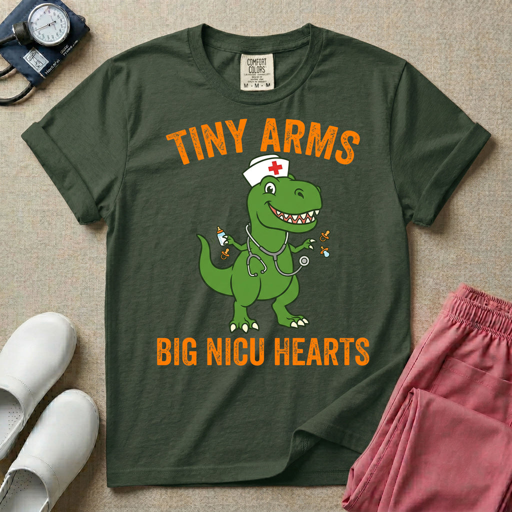 A funny neonatal intensive care unit t-shirt featuring an illustration of a green T-Rex dinosaur wearing a nurse cap and stethoscope, juggling a baby bottle and pacifiers, surrounded by distressed orange text that reads "TINY ARMS" at the top and "BIG NICU HEARTS" at the bottom.