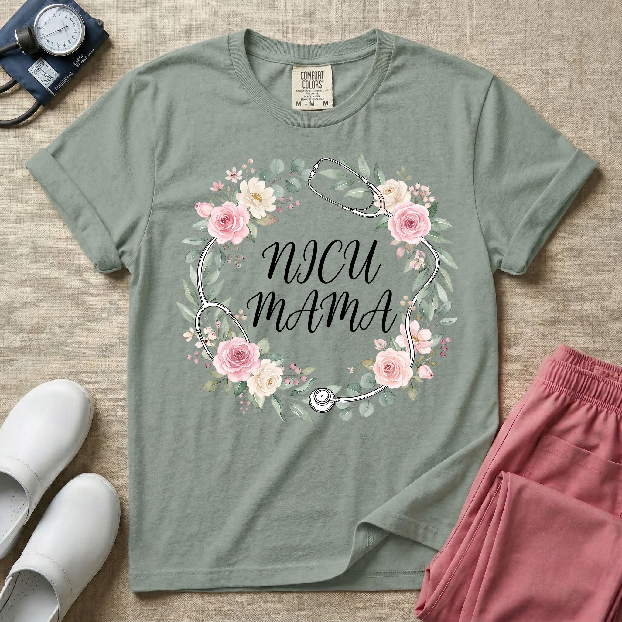 A t-shirt featuring a boho floral wreath composed of pink and cream roses intertwined with a stethoscope, surrounding the text NICU MAMA in elegant typography.
