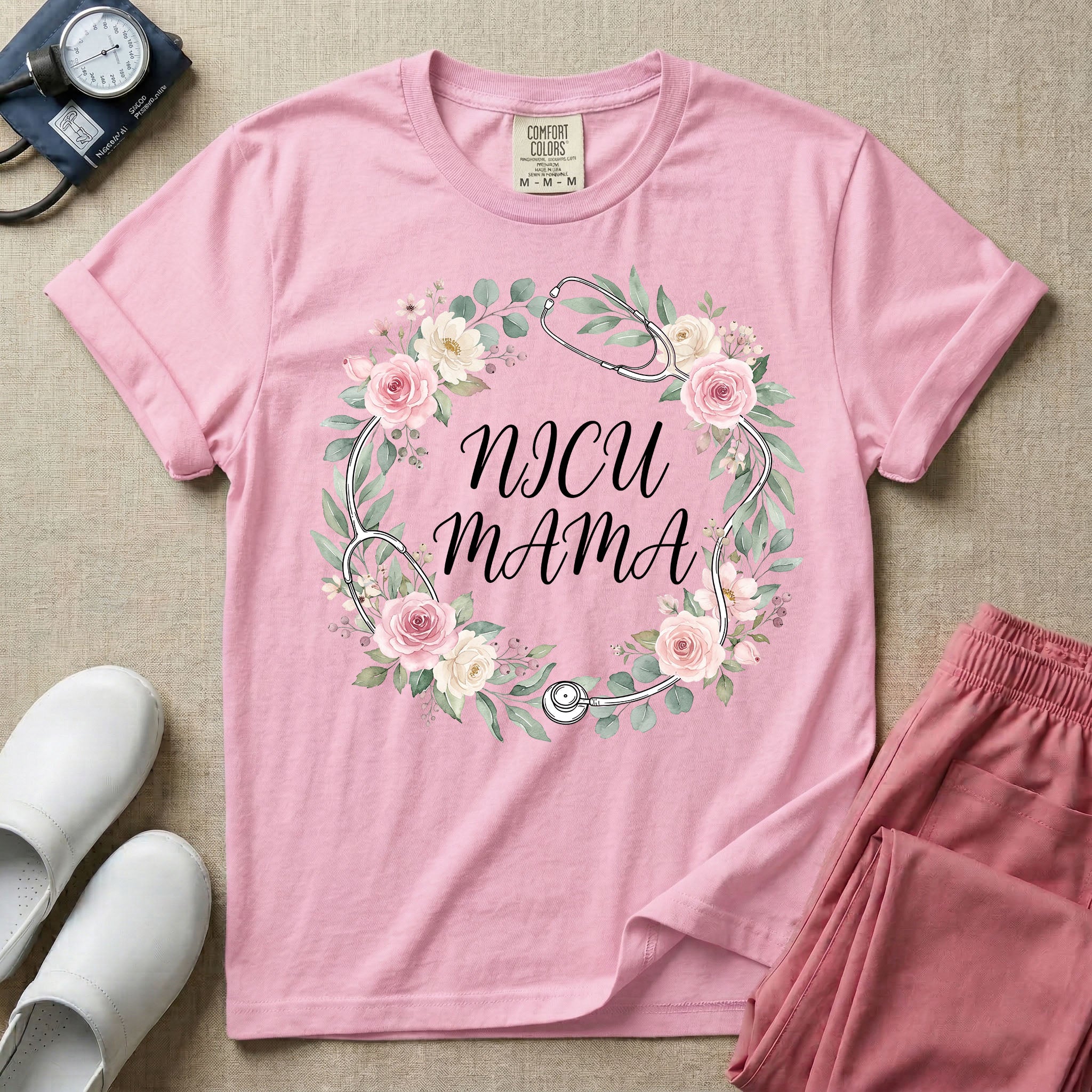 A t-shirt featuring a boho floral wreath composed of pink and cream roses intertwined with a stethoscope, surrounding the text NICU MAMA in elegant typography.