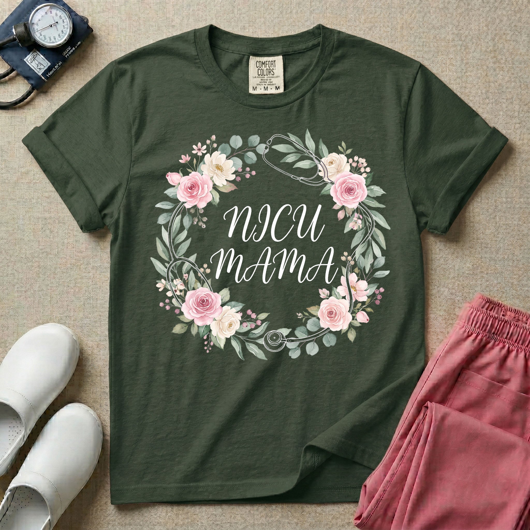 A t-shirt featuring a boho floral wreath composed of pink and cream roses intertwined with a stethoscope, surrounding the text NICU MAMA in elegant typography.