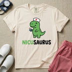 A cute t-shirt for NICU nurses featuring a cartoon green dinosaur wearing a nurse hat with a red cross and holding a blue pacifier above the funny text NICUSAURUS.
