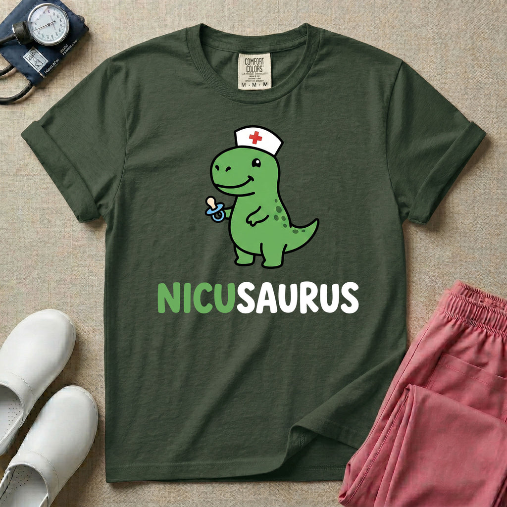 A cute t-shirt for NICU nurses featuring a cartoon green dinosaur wearing a nurse hat with a red cross and holding a blue pacifier above the funny text NICUSAURUS.