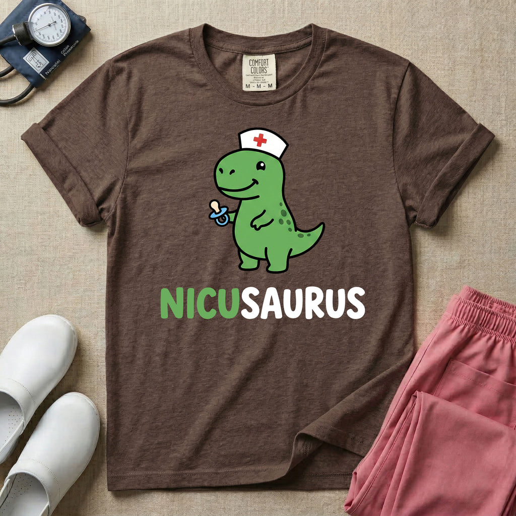 A cute t-shirt for NICU nurses featuring a cartoon green dinosaur wearing a nurse hat with a red cross and holding a blue pacifier above the funny text NICUSAURUS.