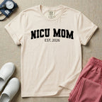 A minimalist personalized t-shirt for the NICU unit featuring bold white collegiate varsity lettering that reads NICU MOM arched over the text EST. 2026.