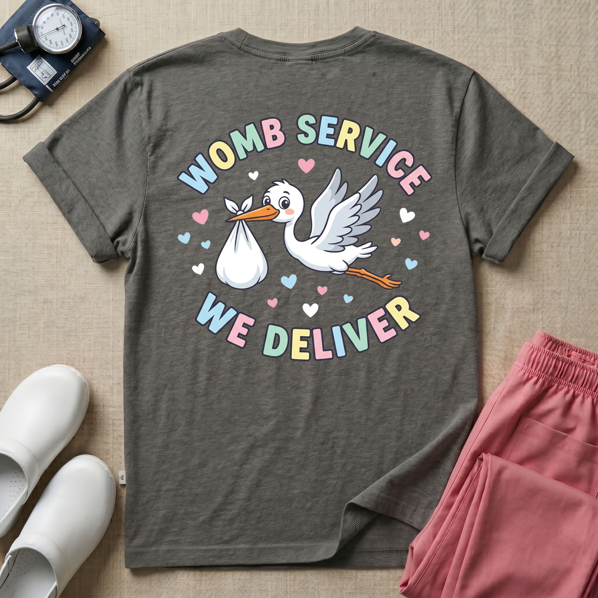 A personalized Labor and Delivery nurse t-shirt featuring a pastel front chest print with the letters L&D above a custom script name Olivia, and a large back print showcasing a cute cartoon stork flying with a baby bundle surrounded by small hearts and the humorous text Womb Service We Deliver.