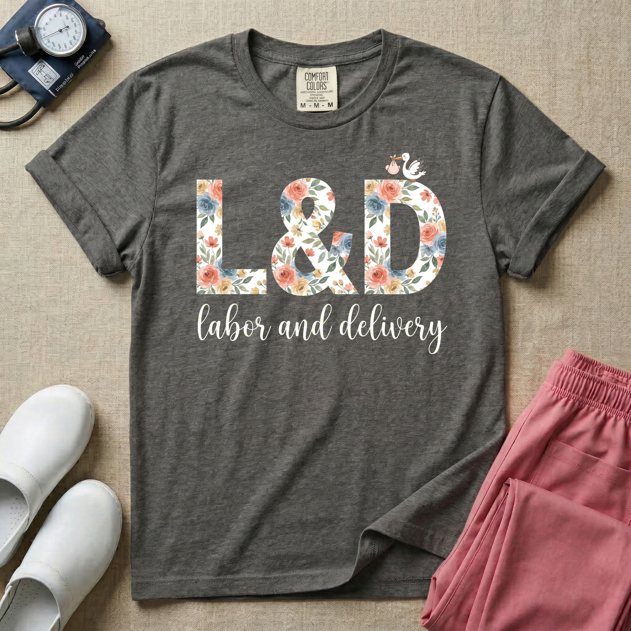 A Labor and Delivery nurse design featuring the large letters L&D filled with a gorgeous boho floral pattern of peach and blue flowers, with a tiny cartoon stork resting on top of the letter D, all positioned above the elegant white script text labor and delivery.