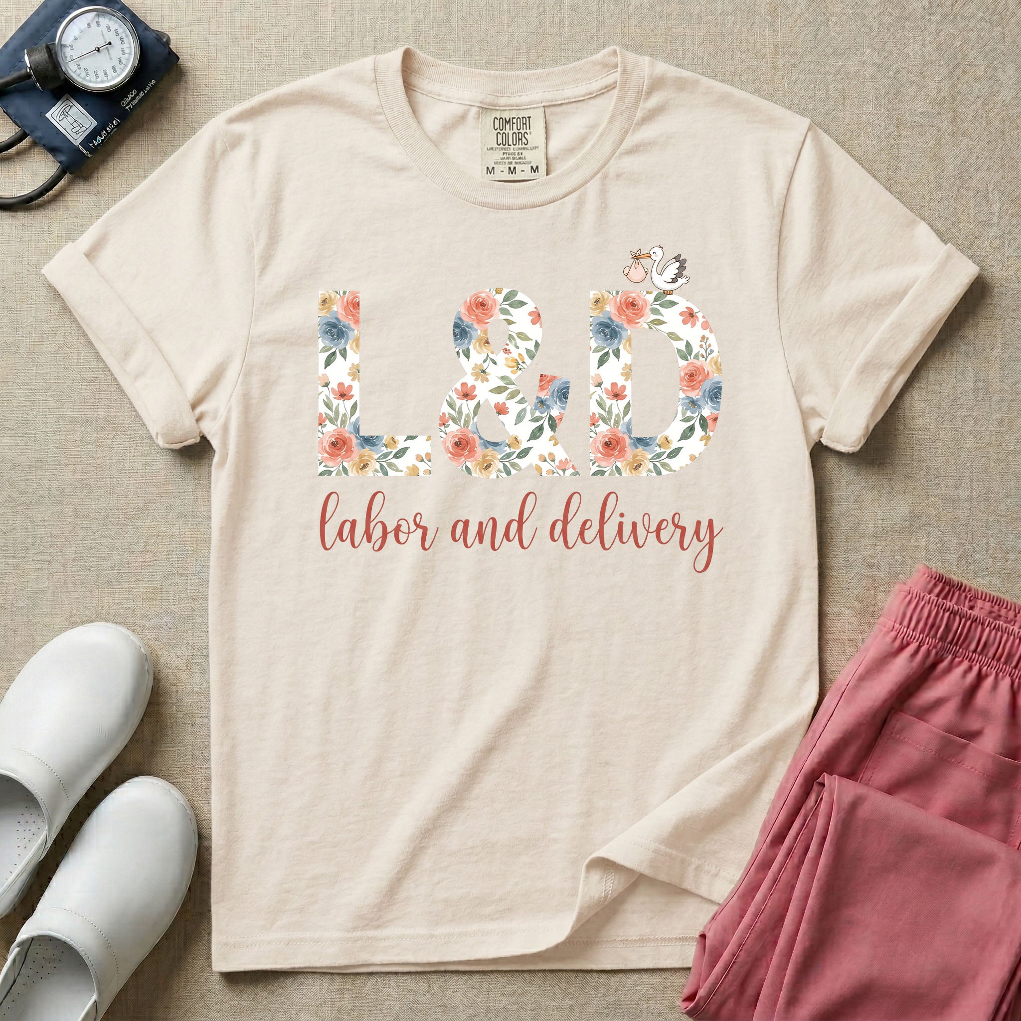 A Labor and Delivery nurse design featuring the large letters L&D filled with a gorgeous boho floral pattern of peach and blue flowers, with a tiny cartoon stork resting on top of the letter D, all positioned above the elegant white script text labor and delivery.