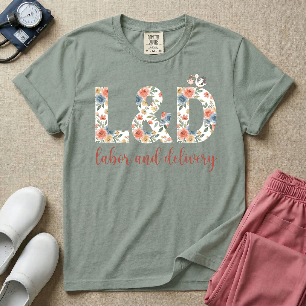 A Labor and Delivery nurse design featuring the large letters L&D filled with a gorgeous boho floral pattern of peach and blue flowers, with a tiny cartoon stork resting on top of the letter D, all positioned above the elegant white script text labor and delivery.
