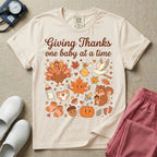 Retro Labor and Delivery and NICU nurse Thanksgiving design reading Giving Thanks One Baby At A Time surrounded by a cute turkey, baby delivery stork, smiling maple leaf, squirrel, pumpkin, baby bottle, booties, and autumn leaves.