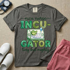 Cute and funny NICU nurse design featuring the text Incu-Gator Tiny But Mighty with an adorable baby alligator swaddled in a hospital receiving blanket resting inside an incubator isolette.