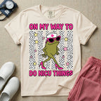 Funny NICU nurse design featuring the text On My Way To Do NICU Things with a sassy frog wearing high heels, sunglasses, and a nurse cap strutting across spotted vertical stripes and stars.