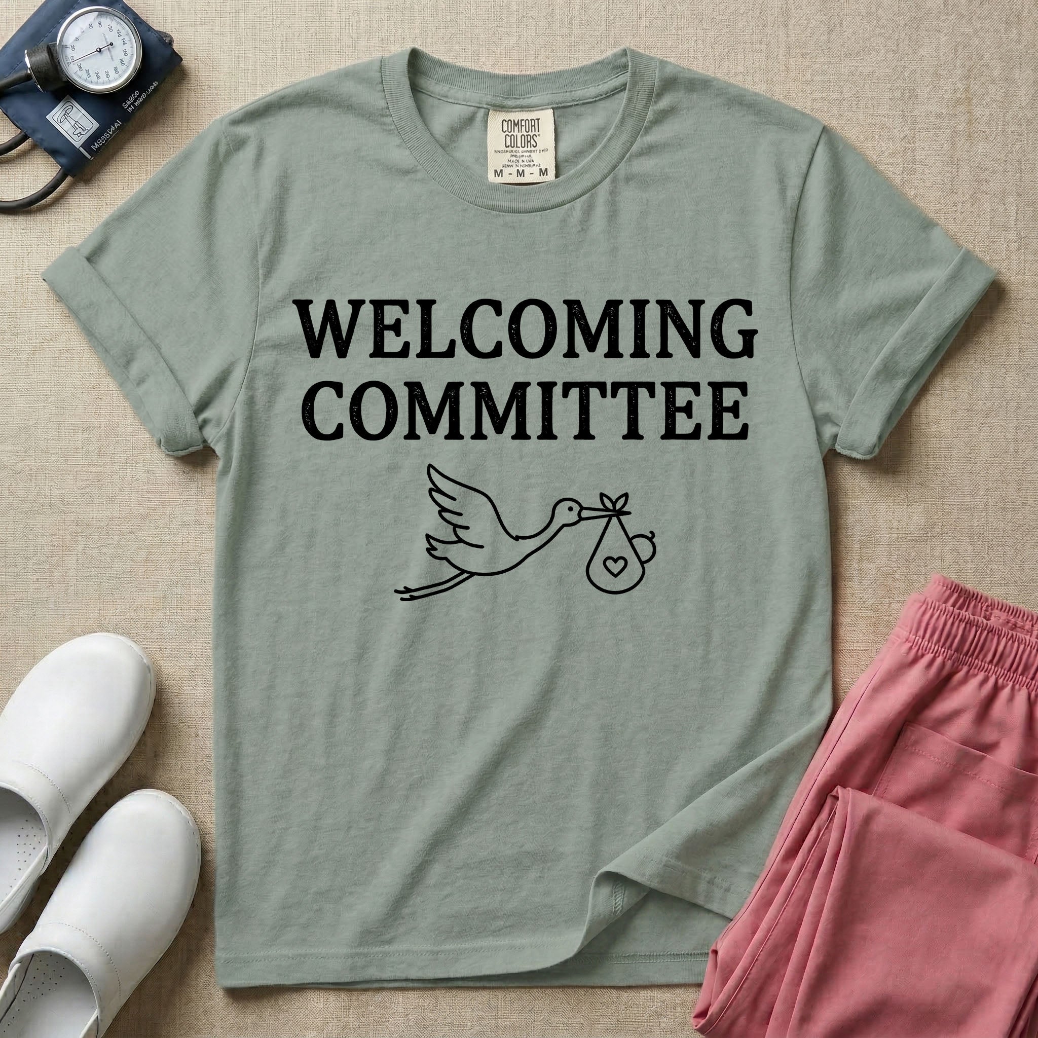 Labor and Delivery nurse graphic featuring a simple white outline of a flying stork carrying a baby bundle with a heart, placed below the text WELCOMING COMMITTEE.
