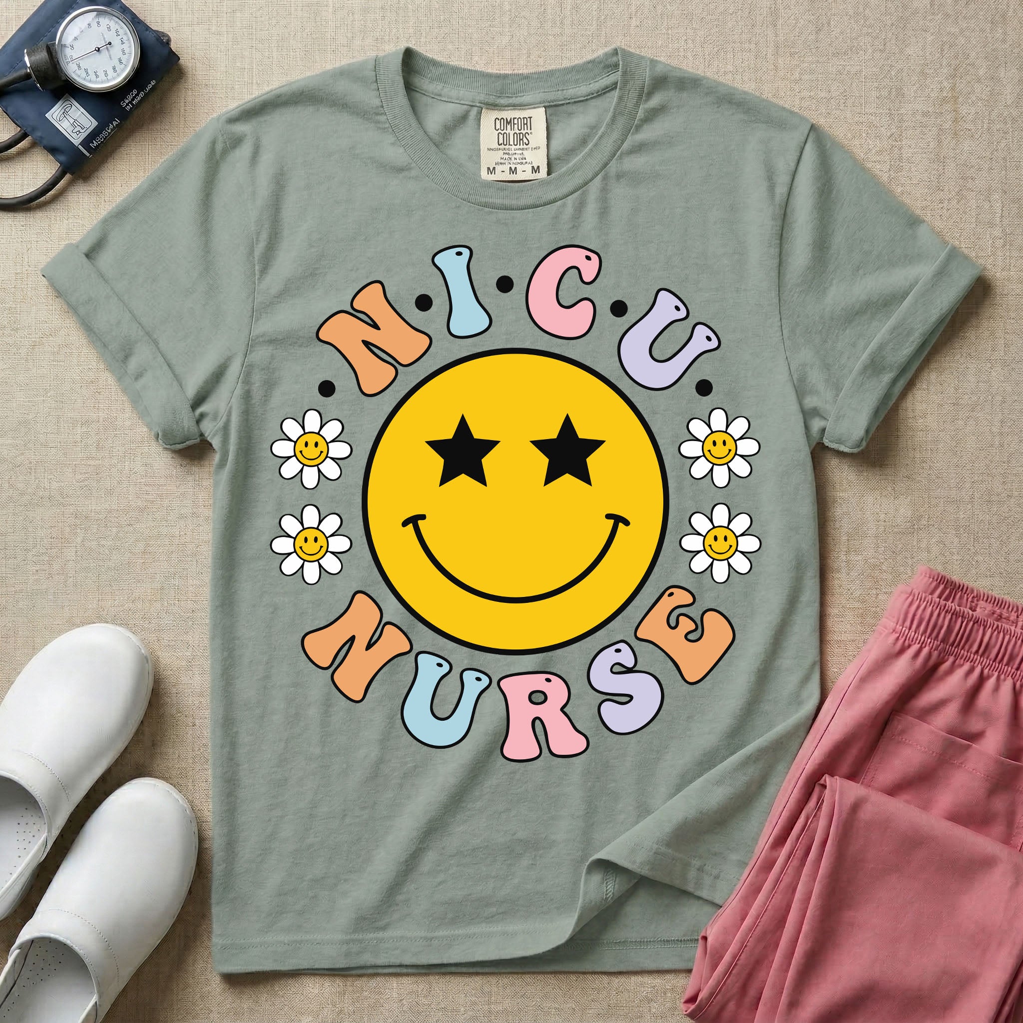 A t-shirt featuring a large yellow smiley face with star eyes surrounded by smiley face daisies and the text N.I.C.U. NURSE in pastel retro bubble lettering.