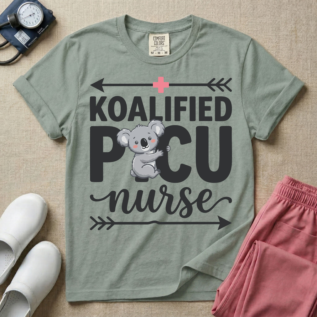 A funny pediatric intensive care nursing t-shirt featuring the pun text "KOALIFIED PICU nurse" with a cute koala graphic replacing the letter I in PICU, framed by decorative arrows and a pink medical cross.