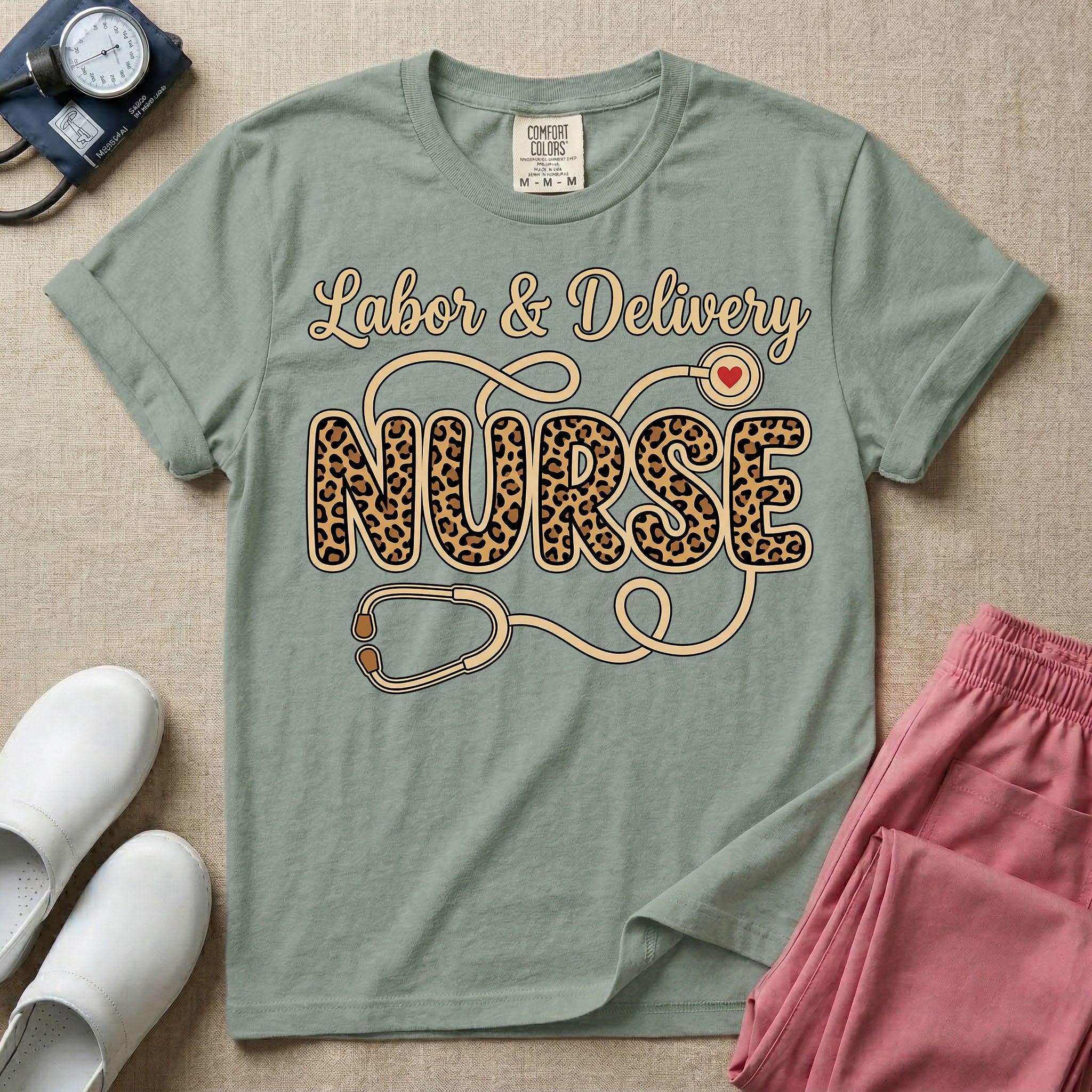 A graphic t-shirt for a Labor and Delivery unit featuring the text 'Labor & Delivery' in beige script above the word 'NURSE' in large leopard print letters, intertwined with an illustration of a stethoscope that features a small red heart on the chest piece.