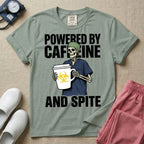 A humorous graphic for general nursing featuring an illustration of a skeleton wearing a green scrub cap and dark blue scrubs, holding a large white coffee cup with a yellow biohazard symbol, with the stacked text 'POWERED BY CAFFEINE' above it and 'AND SPITE' below it.
