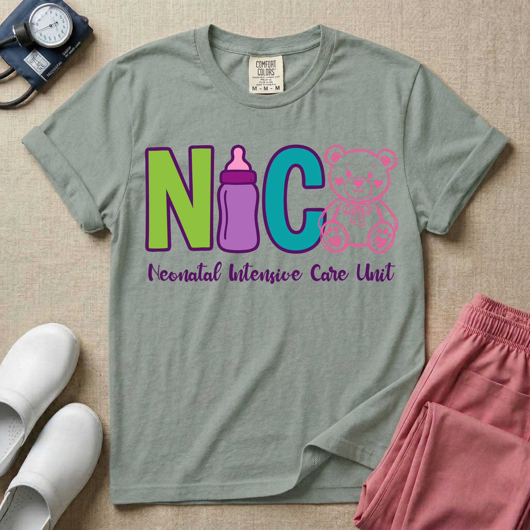A t-shirt featuring the acronym NICU creatively spelled out using a green letter N, a purple baby bottle, a teal letter C, and a pink outlined teddy bear, with the words Neonatal Intensive Care Unit written in cursive script below.