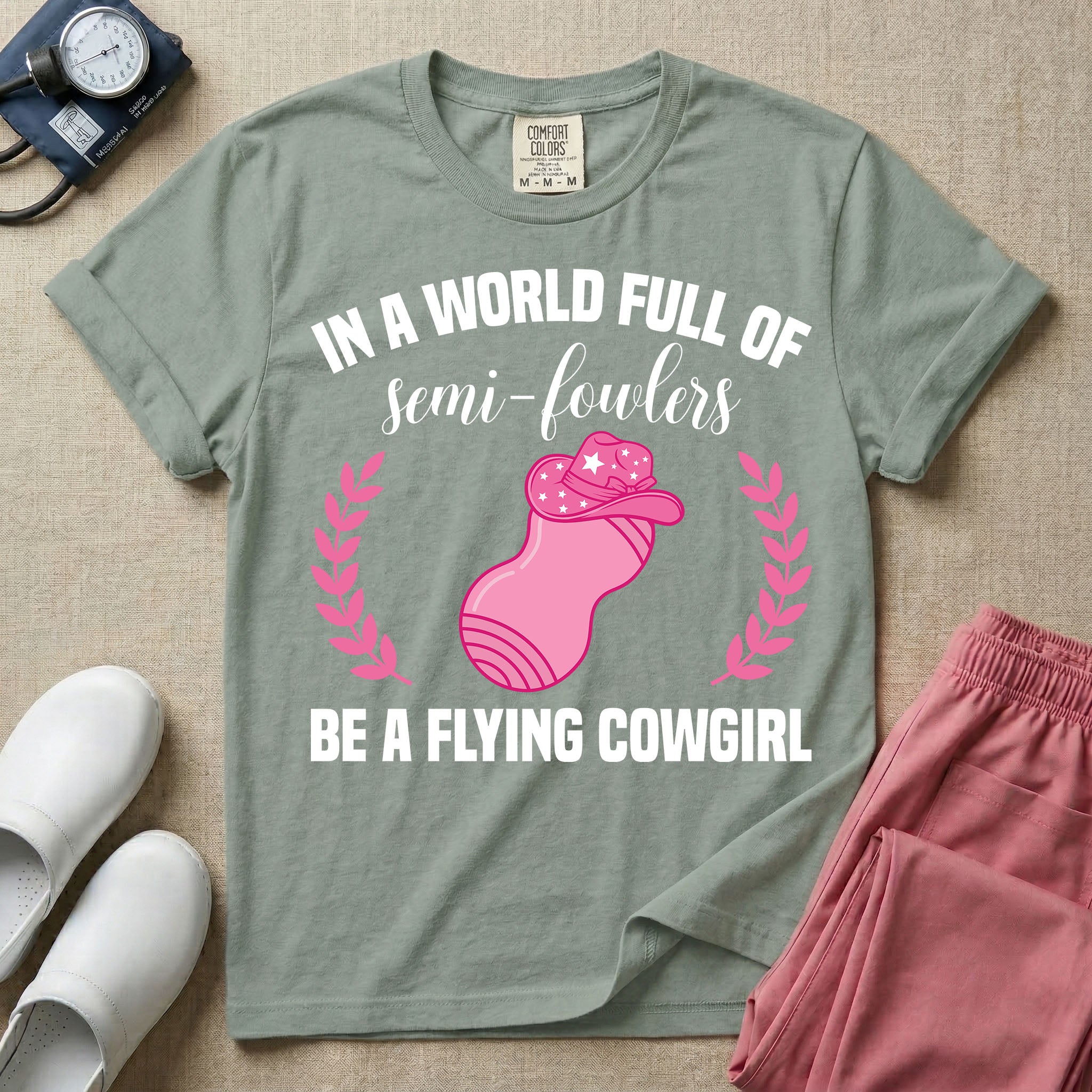 A humorous graphic tee for labor and delivery nurses featuring an illustration of a peanut ball wearing a cowboy hat, framed by laurel branches, along with the text "IN A WORLD FULL OF semi-fowlers BE A FLYING COWGIRL".