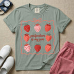 A funny and cute postpartum nursing t-shirt featuring the pun text "postpartum is my jam" surrounded by a graphic of red and pink strawberries, enclosed in a decorative wavy border with a bow at the top.