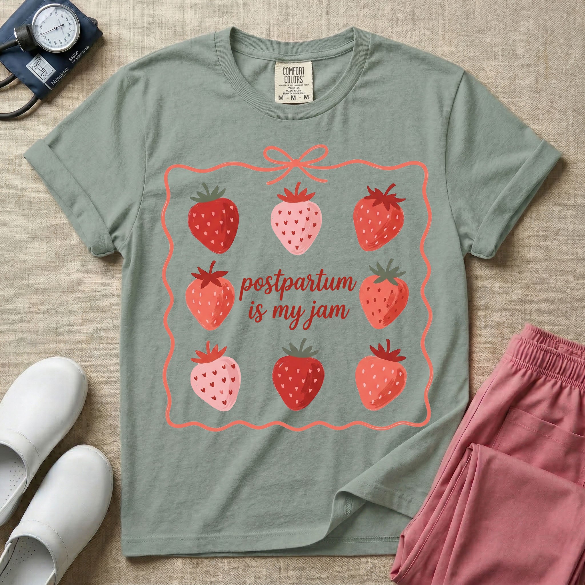 A funny and cute postpartum nursing t-shirt featuring the pun text "postpartum is my jam" surrounded by a graphic of red and pink strawberries, enclosed in a decorative wavy border with a bow at the top.