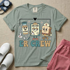 A retro-style t-shirt for emergency room nurses featuring the text "ER CREW" below a vintage cartoon illustration of a medicine bottle, a grumpy clipboard holding an AMA form, and a sandwich wearing a nurse cap walking together.