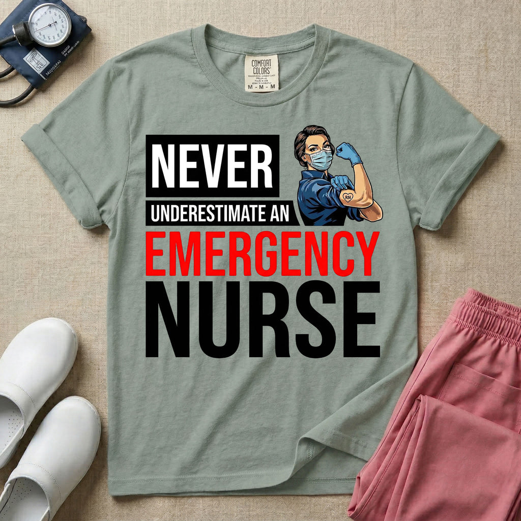 A retro ER nursing t-shirt featuring the bold text "NEVER UNDERESTIMATE AN EMERGENCY NURSE" alongside a vintage graphic of a masked nurse flexing her arm in a classic Rosie the Riveter pose