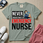 A retro ER nursing t-shirt featuring the bold text "NEVER UNDERESTIMATE AN EMERGENCY NURSE" alongside a vintage graphic of a masked nurse flexing her arm in a classic Rosie the Riveter pose