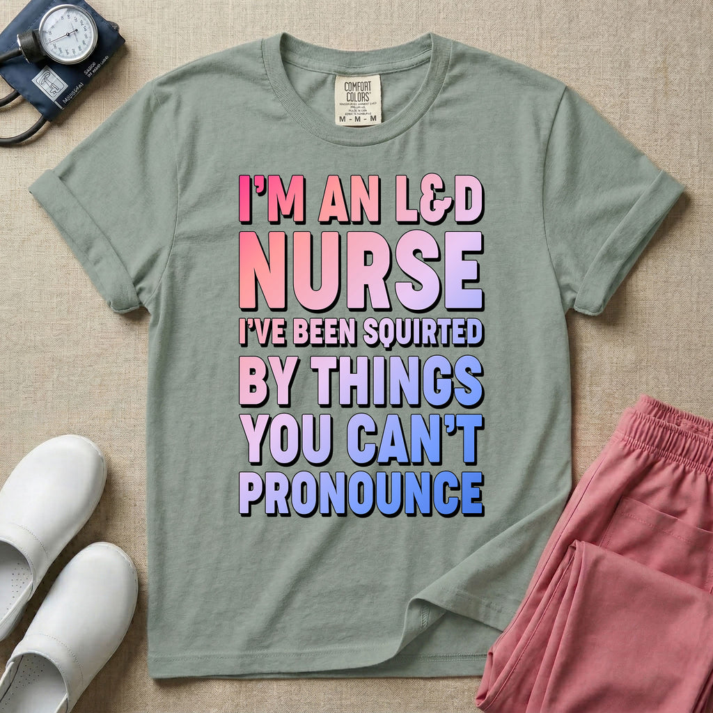 A humorous graphic tee for labor and delivery nurses featuring bold, gradient block lettering that reads "I'M AN L&D NURSE I'VE BEEN SQUIRTED BY THINGS YOU CAN'T PRONOUNCE".