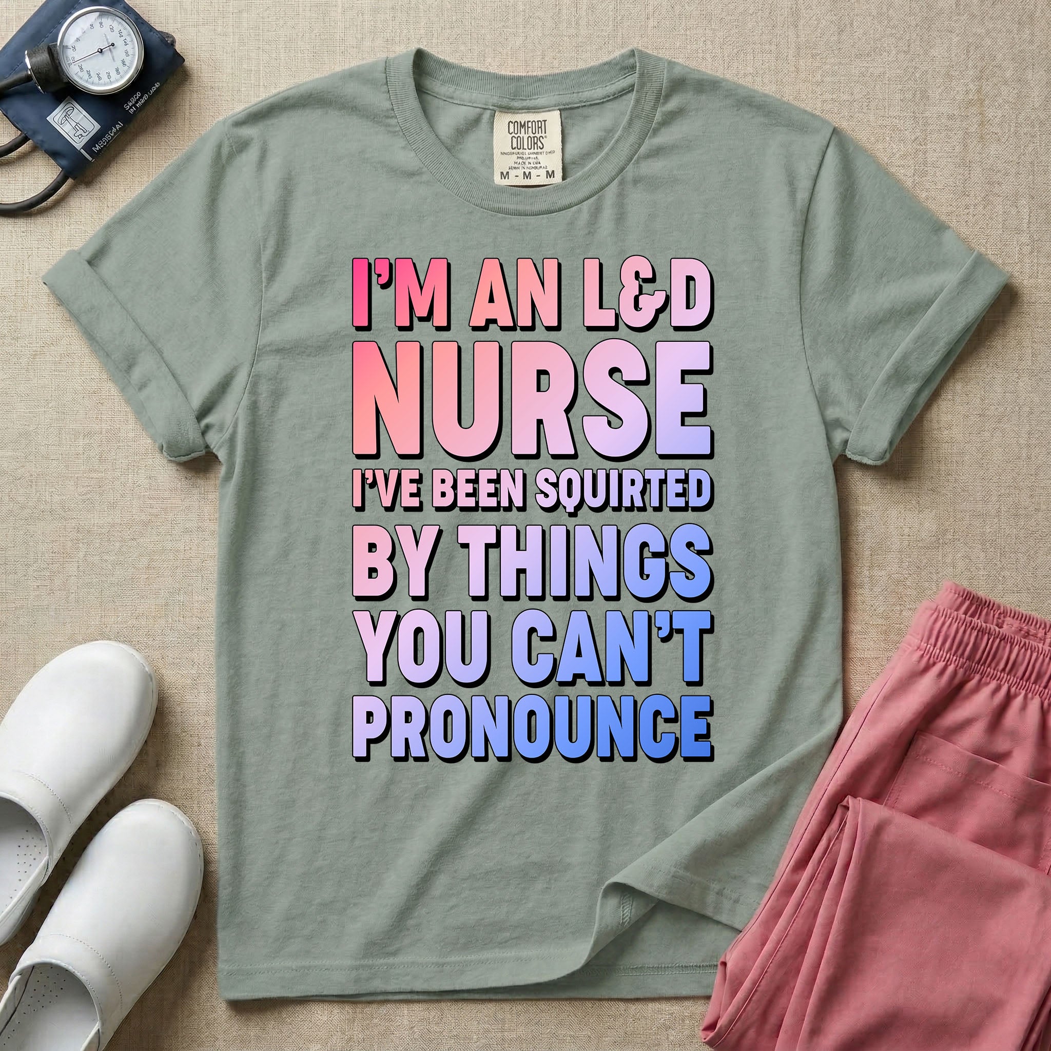 A humorous graphic tee for labor and delivery nurses featuring bold, gradient block lettering that reads "I'M AN L&D NURSE I'VE BEEN SQUIRTED BY THINGS YOU CAN'T PRONOUNCE".