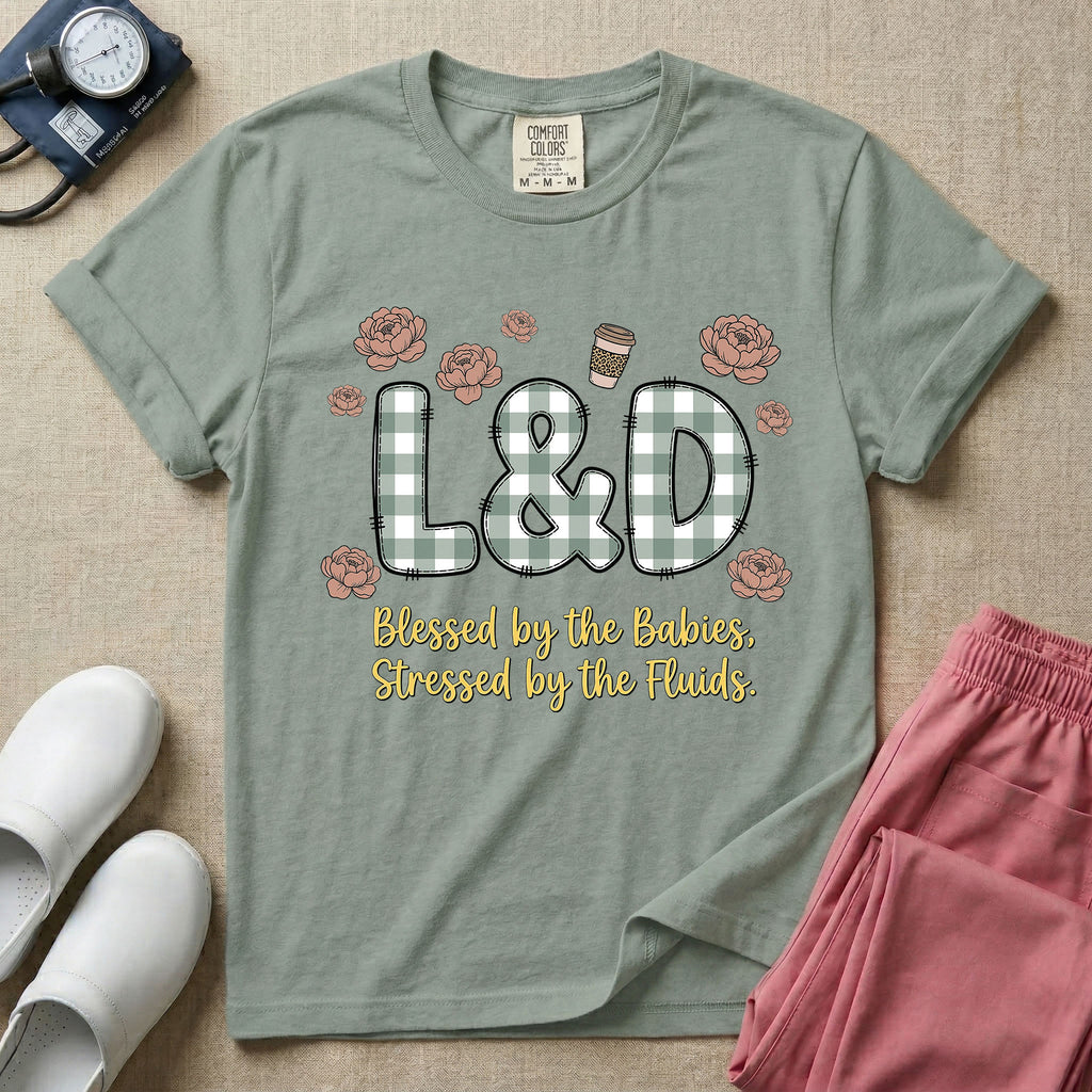 A descriptive graphic tee for labor and delivery nurses featuring plaid block letters spelling L&D surrounded by floral elements and a coffee cup, with the text "Blessed by the Babies, Stressed by the Fluids."