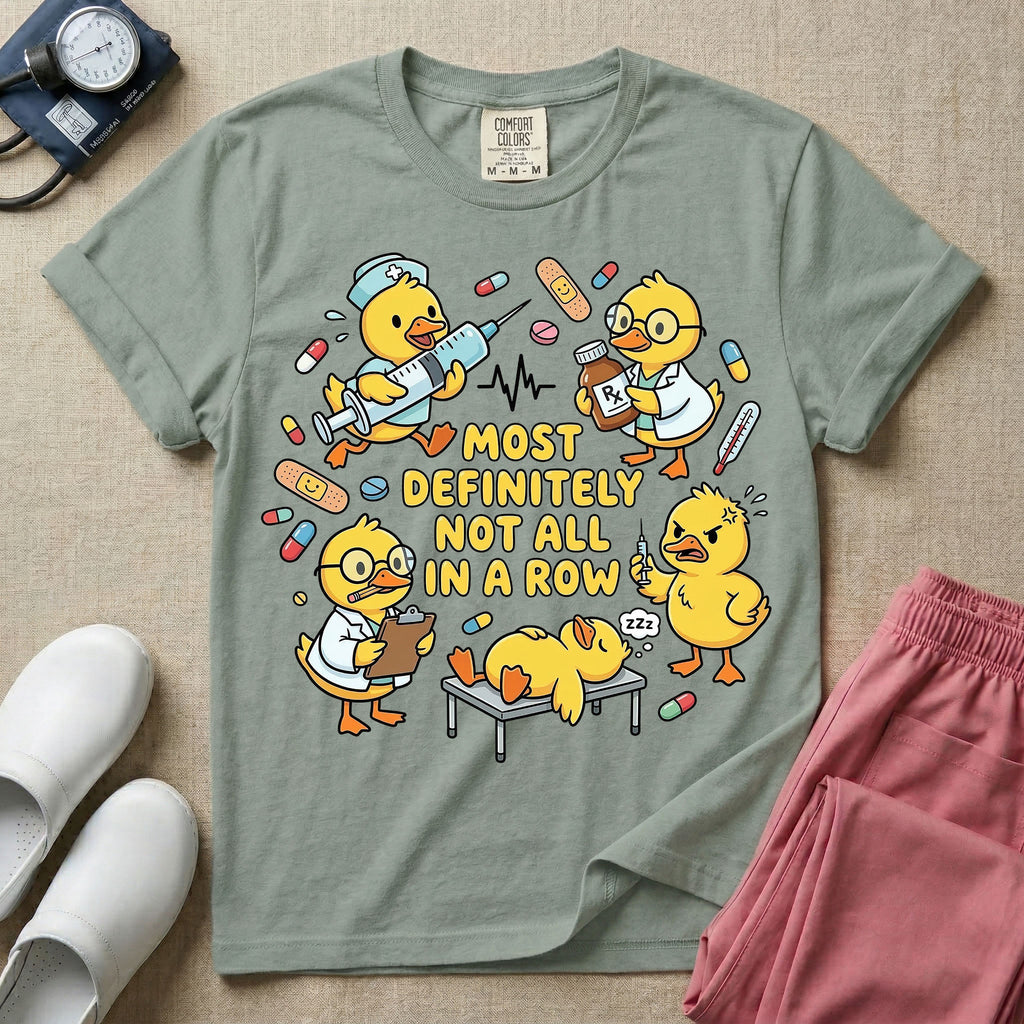 General nursing t-shirt featuring a chaotic group of cartoon ducklings dressed as medical professionals with the text "MOST DEFINITELY NOT ALL IN A ROW" on a sage green garment, in bay color.