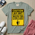 A humorous graphic tee for labor and delivery nurses featuring a distressed caution sign design with the text "CAUTION L&D UNIT: ENTER AT YOUR OWN RISK. WATCH FOR FLYING FLUIDS AND UNFILTERED SCREAMS." above a stick figure nurse holding a shield.