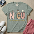 A humorous t-shirt for NICU nurses featuring the large text "NICU" in plaid and patterned letters with the phrase "Tiny Humans. Massive Attitudes." underneath, accompanied by small cute graphics of a syringe, an iced coffee cup, and a baby's face.