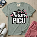 A descriptive graphic tee for pediatric intensive care nurses featuring the text "Team PICU" in bold white lettering, accented with pink hearts and a pink stethoscope design.