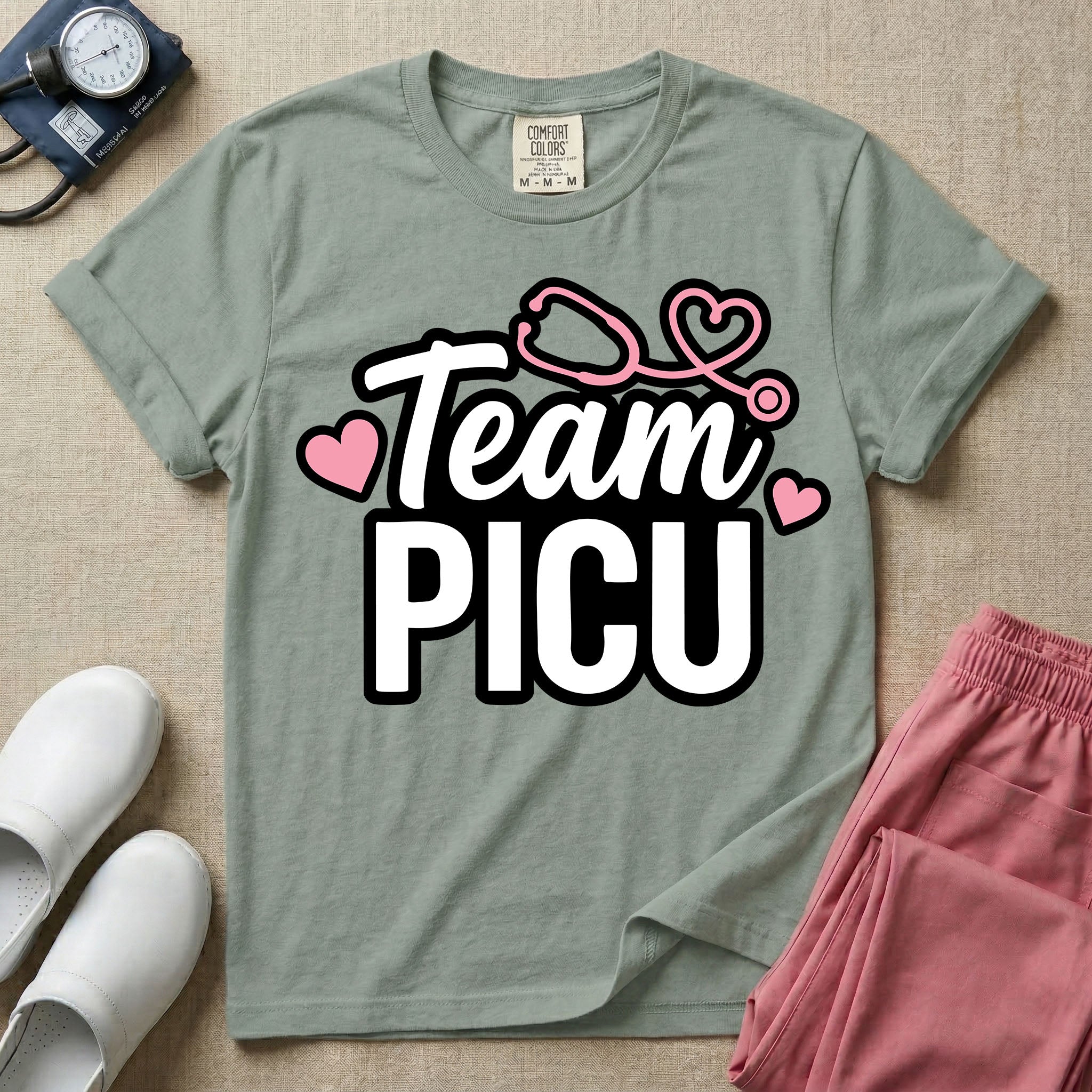 A descriptive graphic tee for pediatric intensive care nurses featuring the text "Team PICU" in bold white lettering, accented with pink hearts and a pink stethoscope design.