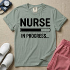 General nursing student t-shirt featuring a white loading bar graphic and the text "NURSE IN PROGRESS..." on a dark gray garment, in bay color.