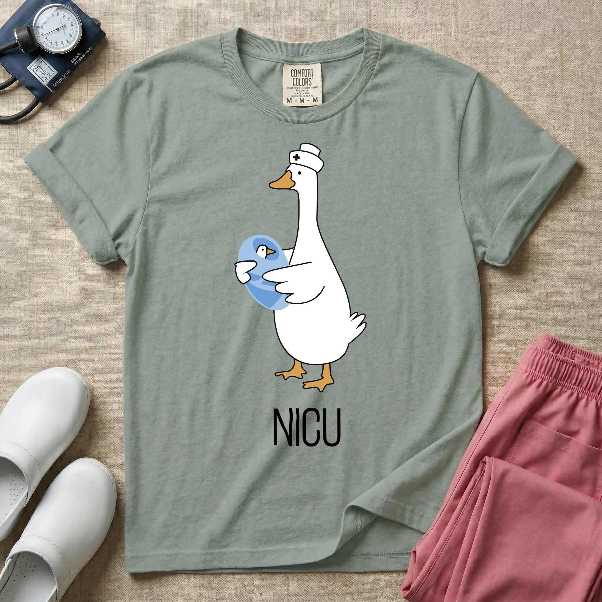 A t-shirt featuring an illustration of a white silly goose wearing a nurse's cap and holding a baby goose swaddled in a blue blanket, with the text NICU printed below.