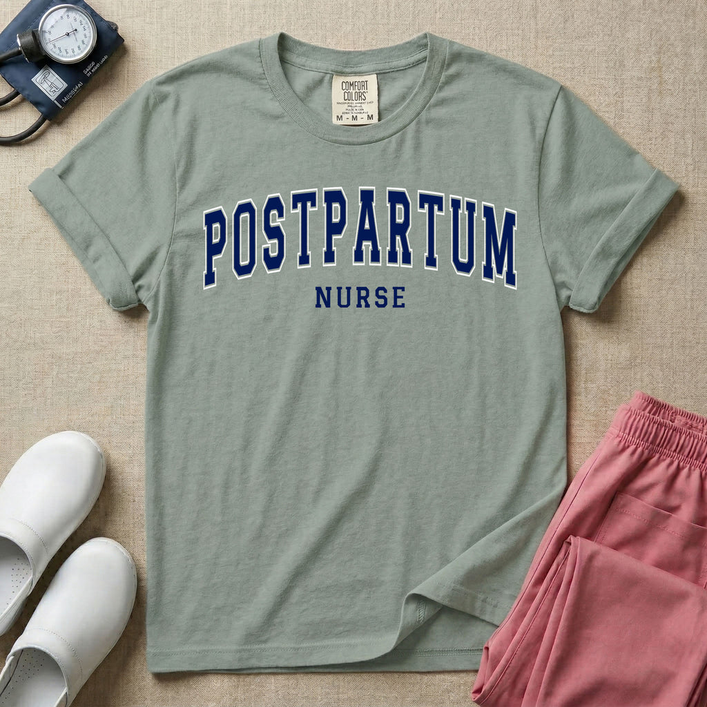 A t-shirt featuring the word POSTPARTUM arched in large collegiate block letters above the word NURSE in a smaller, matching font.