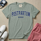 A t-shirt featuring the word POSTPARTUM arched in large collegiate block letters above the word NURSE in a smaller, matching font.