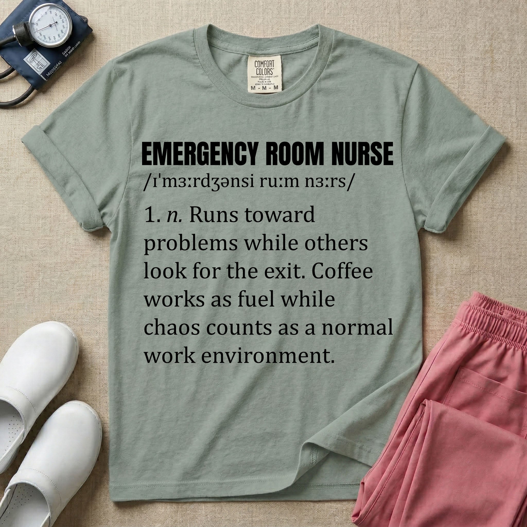 A minimalist t-shirt for emergency room nurses featuring a dictionary definition graphic for the term "EMERGENCY ROOM NURSE" with a phonetic pronunciation and a humorous description about running toward problems, using coffee as fuel, and thriving in chaos.
