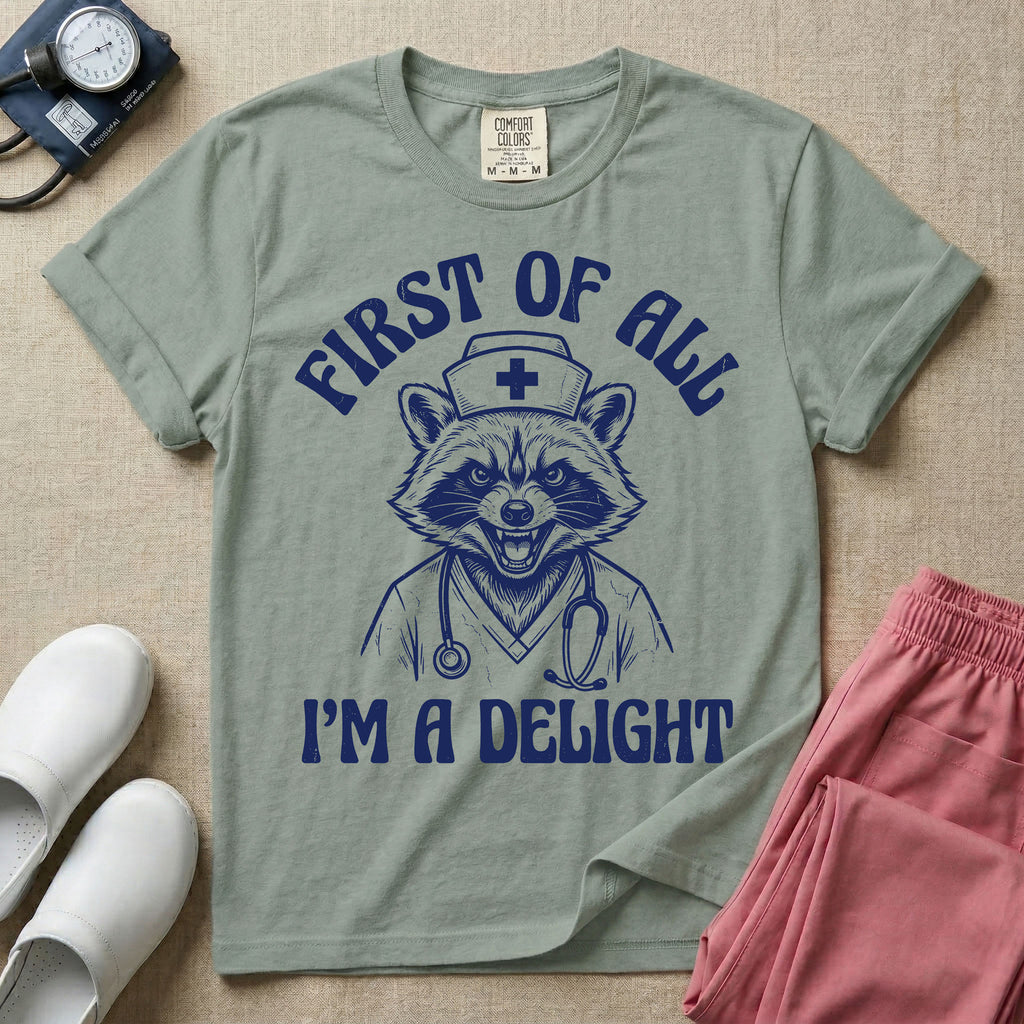 A humorous graphic of a raccoon dressed in a nursing cap and scrub jacket with a stethoscope, with the text "FIRST OF ALL I'M A DELIGHT", in bay color.