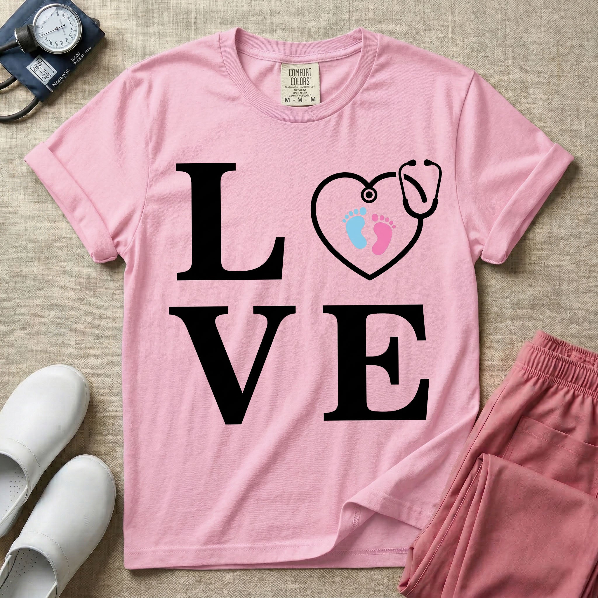 A minimalist nursing t-shirt featuring the word LOVE stacked in large white serif letters, with the letter O replaced by a white stethoscope shaped like a heart containing two small baby footprints, one pink and one blue.