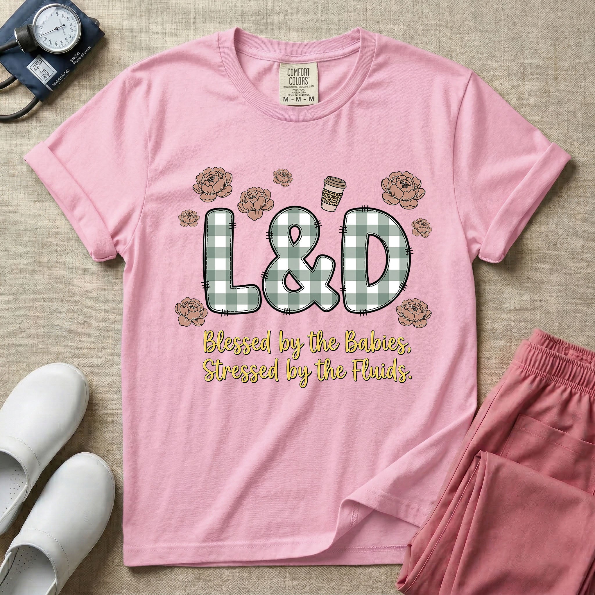 A descriptive graphic tee for labor and delivery nurses featuring plaid block letters spelling L&D surrounded by floral elements and a coffee cup, with the text "Blessed by the Babies, Stressed by the Fluids."