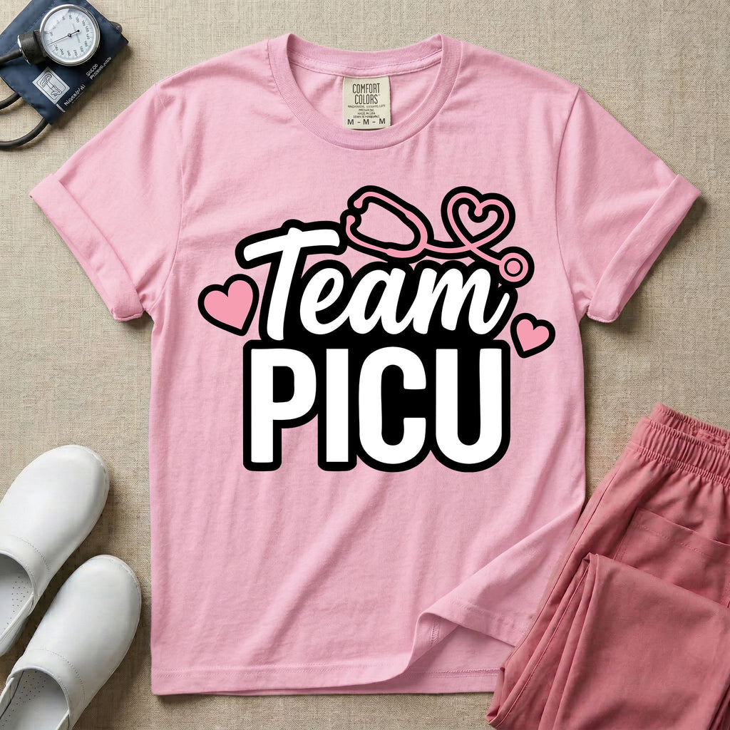 A descriptive graphic tee for pediatric intensive care nurses featuring the text "Team PICU" in bold white lettering, accented with pink hearts and a pink stethoscope design.