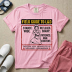 A humorous and retro graphic tee for labor and delivery nurses featuring a vintage nurse illustration alongside the text "FIELD GUIDE TO L&D", "STANCE: WIDE", "REFLEXES: SHARP", "PATIENCE: NON-EXISTENT", and "CAUTION: HIGH PROBABILITY OF UNPLANNED HYDROMASSAGE".